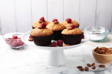 Fresh muffins with raspberries, almonds and flour on white marble table, closeup