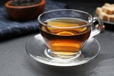 Aromatic tea in glass cup, brown sugar and dried leaves on black table, closeup