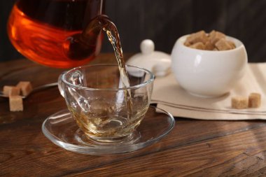Pouring aromatic black tea into glass cup at wooden table, closeup
