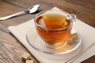 Aromatic black tea in glass cup and brown sugar on wooden table, closeup. Space for text