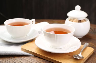 Aromatic black tea in cups and brown sugar on wooden table, closeup