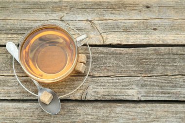 Aromatic black tea in glass cup, brown sugar and spoon on wooden table, top view. Space for text