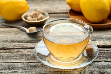 Aromatic black tea in glass cup, brown sugar and lemons on wooden table, closeup
