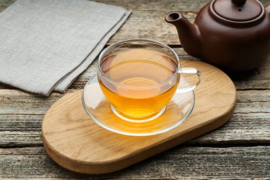 Aromatic black tea in glass cup and teapot on wooden table, closeup