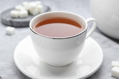 Aromatic black tea in cup and sugar on light grey table, closeup