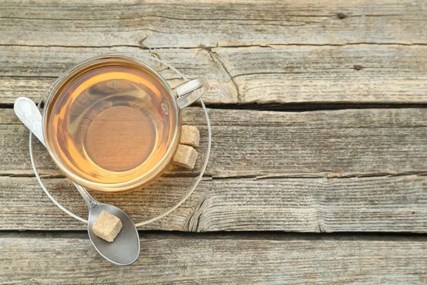 Aromatic black tea in glass cup, brown sugar and spoon on wooden table, top view. Space for text