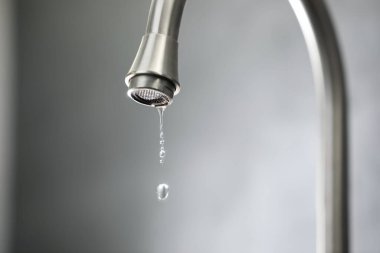 Su tasarrufu konsepti. Gri arka planda musluktan su damlıyor, yakın plan. Metin için boşluk