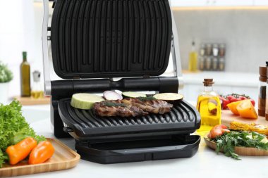 Mutfaktaki beyaz masada lezzetli et, sebze ve baharatla elektrikli ızgara.