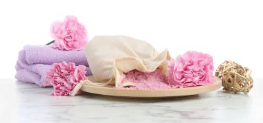 Pink sea salt in bag, towel and beautiful carnation flowers on marble table against white background