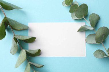 Blank card and eucalyptus branches on light blue background, flat lay