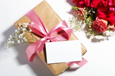 Blank card, gift box and beautiful flowers on white background, flat lay