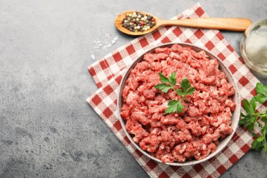 Raw minced meat with parsley and spices on grey table, flat lay. Space for text