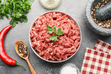 Raw minced meat with parsley and spices on grey table, flat lay