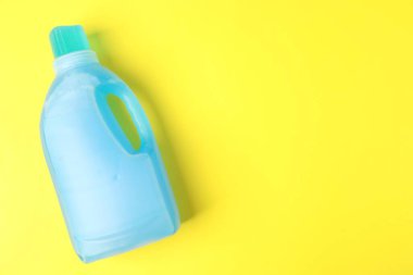 Bottle of laundry detergent on yellow background, top view. Space for text