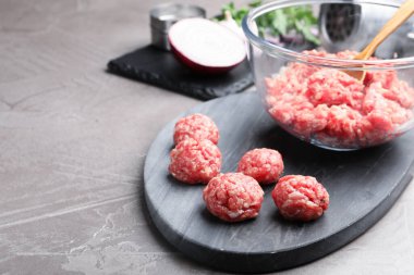 Raw meatballs and minced meat on grey table, closeup. Space for text