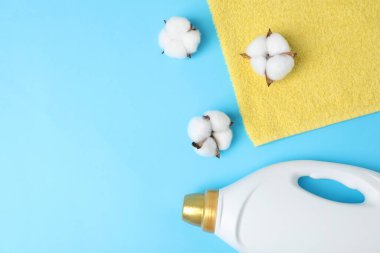 Bottle of fabric softener, towel and cotton flowers on light blue background, flat lay. Space for text