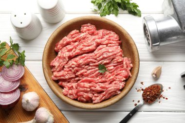 Raw minced meat, parsley, spices and grinder on white wooden table, flat lay