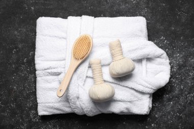 Composition with bathrobe, herbal bags and brush on black background, top view. Spa and relax