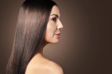 Koyu kahverengi arka planda güzel, parlak, pürüzsüz saçları olan bir kadın.