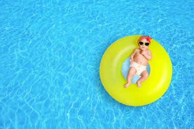 Güneş gözlüklü şirin bir bebek ve yüzme havuzunda sarı şişirilebilir bir yüzük. Üst görünüm