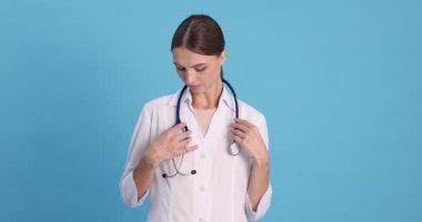 Açık mavi arka planda steteskobu olan profesyonel hemşire, kamera geliyor.