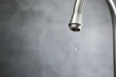 Su tasarrufu konsepti. Gri arka planda musluktan su damlıyor, yakın plan. Metin için boşluk