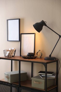 Stylish lamp, other decor and books on console table near beige wall indoors