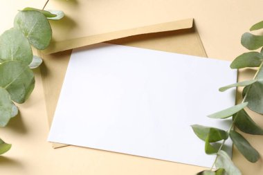 Blank card, envelope and eucalyptus branches on beige background, above view