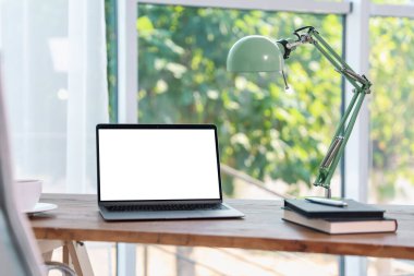 Boş beyaz ekranlı dizüstü bilgisayar, odada lamba ve kırtasiye malzemesi. Rahat ev işyeri