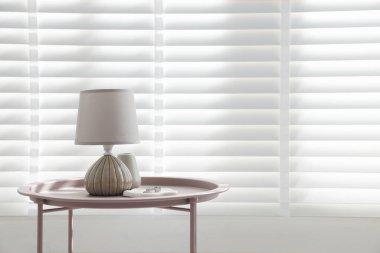 İçerideki pencerenin yanındaki sehpada şık lamba, vazo ve yüzükler var. Metin için boşluk