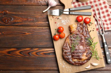 Delicious grilled beef steak with herbs, spices and products on wooden table, flat lay. Space for text