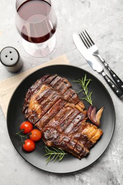 Biberiye, soğan ve domatesli leziz ızgara biftek. Gri desenli masada servis ediliyor.