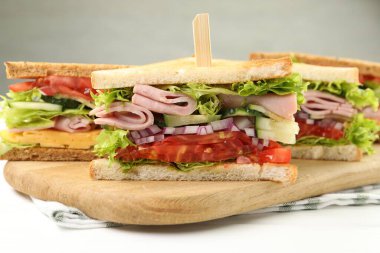 Tasty sandwiches with ham and vegetables on white wooden table, closeup