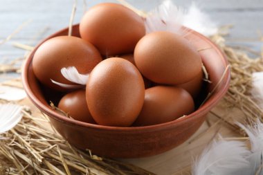 Tabakta çiğ tavuk yumurtası, masada tüy ve saman, yakın plan.