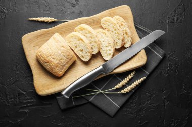 Taze ciabatta parçaları, siyah desenli masa üzerinde bıçak ve buğday kulakları.