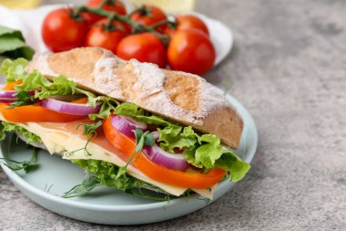 Delicious ciabatta sandwich with prosciutto, cheese and vegetables on light grey table, closeup. Space for text