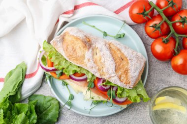 Açık gri masada servis edilen jambonlu, peynirli ve sebzeli lezzetli ciabatta sandviçi.