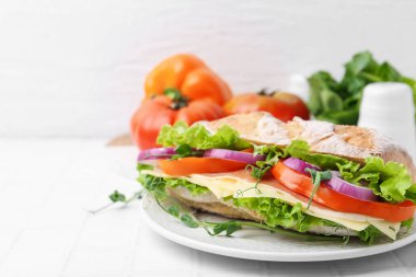 Delicious ciabatta sandwich with prosciutto, cheese and vegetables on white tiled table, closeup. Space for text