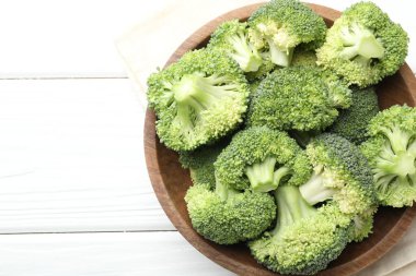 Fresh green broccoli in bowl on white wooden table, top view. Space for text