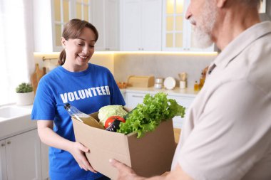 Yaşlılar için insani yardım. Gönüllü, içinde yiyecek olan karton kutuları evin içindeki yaşlı adama veriyor.