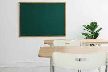 Boş yeşil karatahta, masalar, sandalyeler ve bitkiler sınıfta