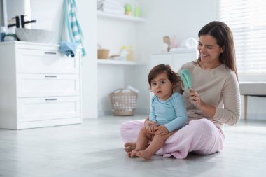 Anne banyoda bebeğinin saçını tarıyor, mesaj atmak için yer açıyor.