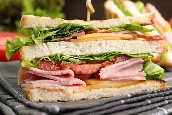 Вкусные бутерброды с ветчиной, беконом, сыром и овощами на столе, крупным планом