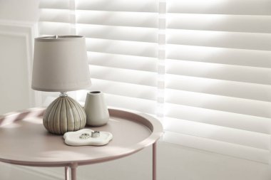 İçerideki pencerenin yanındaki sehpada şık lamba, vazo ve yüzükler var. Metin için boşluk