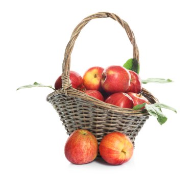 Hasır sepetteki taze elmalar ve beyaz üzerinde yeşil yapraklar.