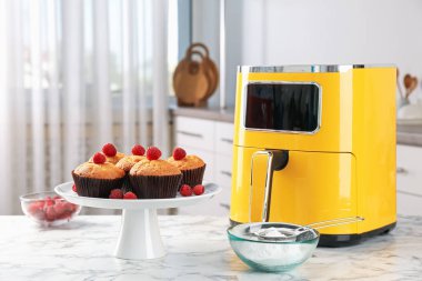 Mutfaktaki beyaz mermer masada ahududu, un ve hava kızartmalı taze pişmiş muffinler.