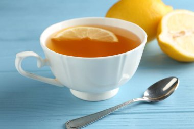 Bardakta romatik çay, açık mavi ahşap masada limon ve kaşık, yakın plan.