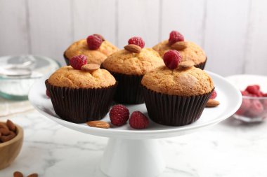 Fresh muffins with raspberries, almonds and flour on white marble table, closeup