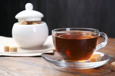 Cam bardakta koyu siyah çay ve ahşap masada kahverengi şeker, yakın plan.