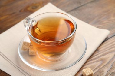 Aromatic black tea in glass cup and brown sugar on wooden table, closeup. Space for text